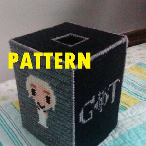 May include: A black and gray tissue box cover with a white and gray pixelated image of a character from the TV show Game of Thrones. The text "GOT" is on the side of the box.
