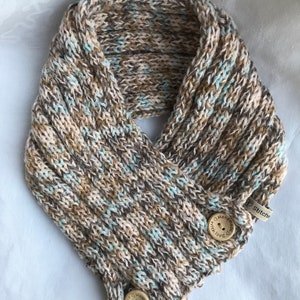 May include: A brown, beige and light blue knitted neck warmer with two wooden buttons that say "Handmade with love".