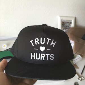 May include: Black and white baseball cap with the text "TRUTH - HEART - HURTS" on the front.