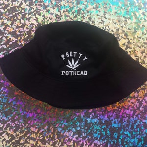May include: Black bucket hat with white embroidery that reads "PRETTY POTHEAD" with a marijuana leaf graphic.