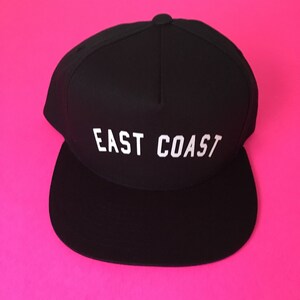 May include: A black and white baseball cap with the text "EAST COAST" embroidered in white on the front.