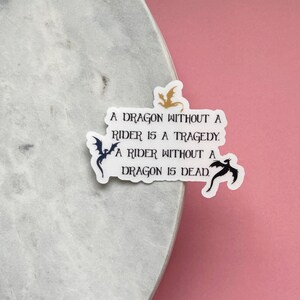 May include: A white sticker with black and gold dragon silhouettes and the text "A dragon without a rider is a tragedy. A rider without a dragon is dead."