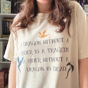 Może przedstawiać: Biały t-shirt z czarnym nadrukiem graficznym, który brzmi: "Smok bez jeźdźca to tragedia. Jeździec bez smoka jest martwy."