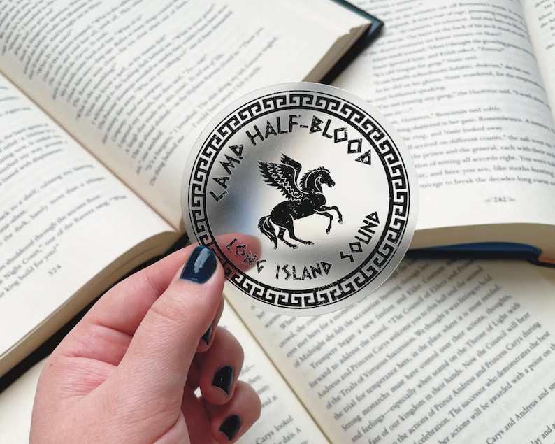 Pu&ograve; includere: Un adesivo rotondo trasparente con testo nero e un'illustrazione di Pegaso nero. Il testo recita "LAMA HALF-BLOOD LONG ISLAND SOUND". L'adesivo &egrave; tenuto sopra un libro aperto.
