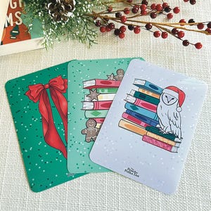 May include: Three Christmas-themed cards with rounded corners. One card features a red bow on a green polka-dotted background. Another shows a stack of books with a gingerbread man. The third card has an owl wearing a Santa hat.
