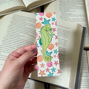 May include: A bookmark featuring a green and blue seahorse with a pink, orange, and blue seashell and starfish pattern. The bookmark has the text "Red Queen" at the bottom.