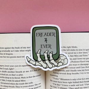 May include: A sticker showing a green e-reader held by a skeleton hand, with the text "EREADER 4 EVER". The sticker is on an open book with printed text.
