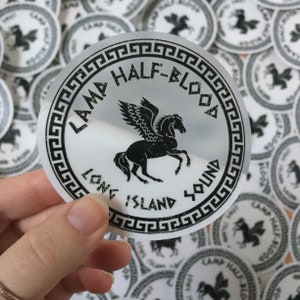 Pu&ograve; includere: Un adesivo rotondo con un'illustrazione di un cavallo alato nero e il testo "Camp Half-Blood Long Island Sound" in un bordo a chiave greca. Altri adesivi sono visibili sullo sfondo.