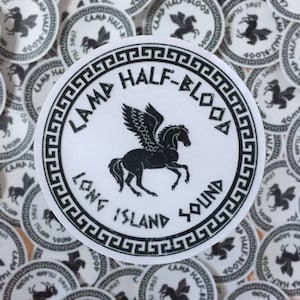 Pu&ograve; includere: Adesivo circolare bianco con testo nero e illustrazione di un cavallo alato. Il testo recita "CAMP HALF-BLOOD LONG ISLAND SOUND". Un bordo a chiave greca incornicia il design.