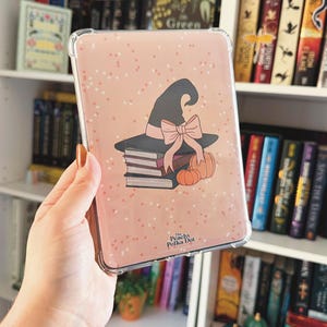 May include: A clear phone case with a pink polka dot design. The case features a witch hat, books, pumpkins, and a bow. The text "Peachy Polka Dot" is visible on the case.