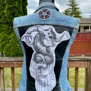May include: A blue denim vest with a black leather patch featuring a hand holding a snake with a skull head. A pentagram patch is on the upper back of the vest.