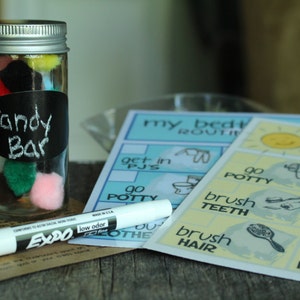 May include: A clear glass jar with a silver lid filled with colorful pom-poms. The jar has a black label that says "Candy Bar". There are two printed cards with the text "my bedtime routine" and "my morning routine" with illustrations of activities like brushing teeth, getting dressed, and going to the bathroom.