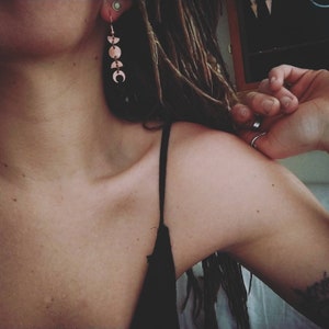 May include: A woman with long brown hair wearing a black tank top and a silver earring with a crescent moon design.