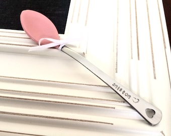 May include: A personalized pink silicone-tipped spoon with a silver handle. The handle is engraved with the name "Aniston" and a heart.