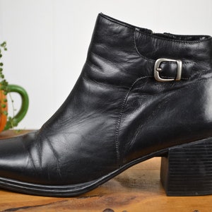 May include: Black leather ankle boots with a buckle detail and a block heel.