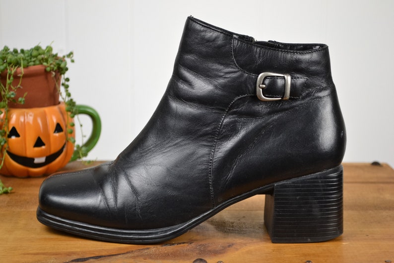 May include: Black leather ankle boots with a buckle detail and a block heel.