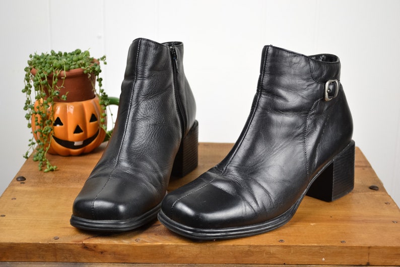 May include: A pair of black leather ankle boots with a block heel. One boot has a buckle closure on the ankle.