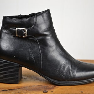 May include: Black leather ankle boots with a buckle detail and a block heel.