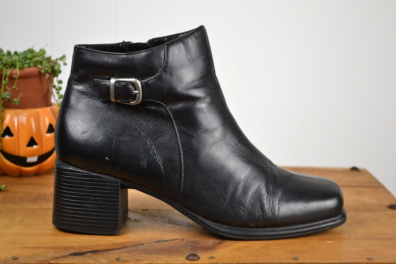 May include: Black leather ankle boots with a buckle detail and a block heel.