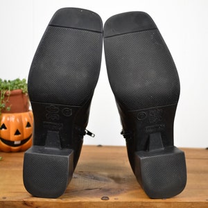 May include: Black leather ankle boots with a zipper on the side and a block heel. The soles of the boots are textured.