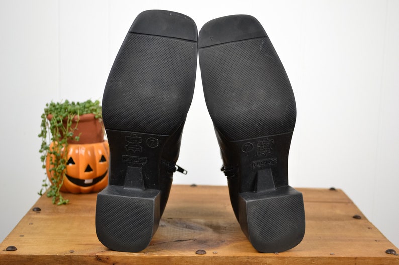 May include: Black leather ankle boots with a zipper on the side and a block heel. The soles of the boots are textured.