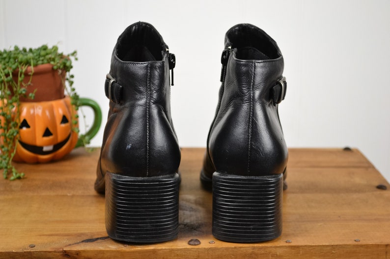 May include: A pair of black leather ankle boots with a chunky heel and buckle detail.