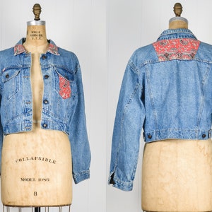 Könnte beinhalten: Eine verkürzte Jeansjacke mit einem roten und weißen Paisley-Muster am Kragen und an der Gesäßtasche. Die Jacke hat eine hellblaue Waschung und ist aus Denim.