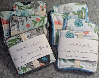 Op de afbeelding: Twee sets vierkante make-up remover pads, elk bestaande uit twee stuks. De pads hebben bloemen- en cactuspatronen in tinten groen, blauw en oranje. Elke set is verpakt in een witte papieren band met het label Buddy Buster and Bug.