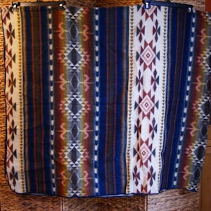 Könnte beinhalten: Eine rechteckige Decke mit einem vertikalen Streifenmuster und geometrischen Rautenmotiven. Die Farbpalette umfasst tiefes Blau, Creme, Dunkelbraun und gedämpfte Rottöne. Das Design besteht aus sich wiederholenden Bändern mit Mustern.
