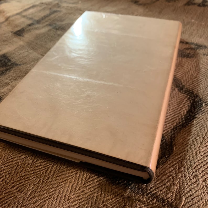 Puede incluir: Un libro de tapa dura de color marr&oacute;n claro con una cubierta lisa y ligeramente texturizada. El libro est&aacute; cerrado y se encuentra sobre una superficie de color marr&oacute;n con un patr&oacute;n.