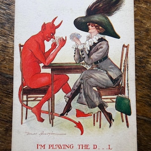 May include: A vintage postcard illustration depicts a red devil with horns and a tail playing cards at a table with a person wearing a large green hat with a feather, a grey coat, and a white ruffled collar. The text reads I'M PLAYING THE D..L.