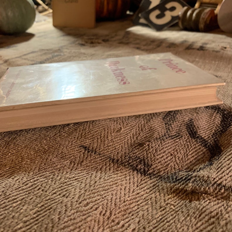 Puede incluir: Un libro blanco con el t&iacute;tulo "Prince of Darkness" impreso en rosa en la portada.