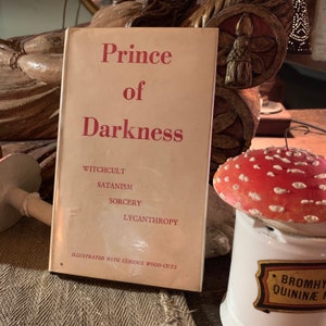 Puede incluir: Un libro vintage titulado "Pr&iacute;ncipe de las Tinieblas" con las palabras "Witchcult, Satanism, Sorcery, Lycanthropy" impresas en la portada. El libro est&aacute; ilustrado con curiosos grabados en madera.