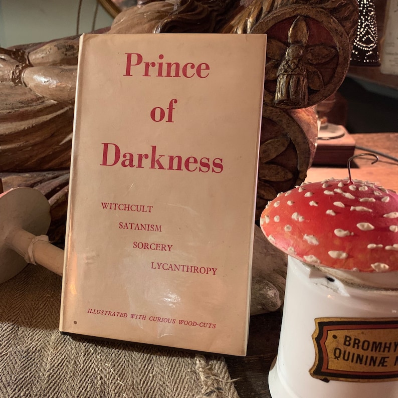 Puede incluir: Un libro vintage titulado "Pr&iacute;ncipe de las Tinieblas" con las palabras "Witchcult, Satanism, Sorcery, Lycanthropy" impresas en la portada. El libro est&aacute; ilustrado con curiosos grabados en madera.