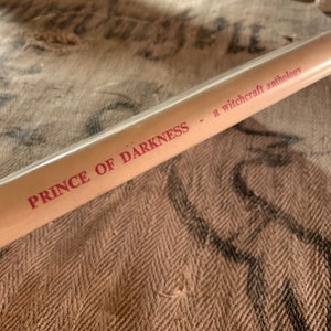 Puede incluir: Primer plano del lomo de un libro titulado "Prince of Darkness - a witchcraft anthology". El t&iacute;tulo est&aacute; impreso en rojo sobre un fondo marr&oacute;n.