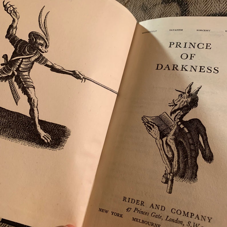 Puede incluir: Una ilustraci&oacute;n en blanco y negro de un demonio sosteniendo un libro. El texto "PRINCE OF DARKNESS" est&aacute; impreso sobre la ilustraci&oacute;n. El texto "RIDER AND COMPANY 47 Princes Gate, London, S.W. MELBOURNE NEW YORK" est&aacute; impreso debajo de la ilustraci&oacute;n.