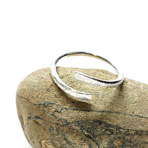 Puede incluir: Un brazalete de plata con acabado texturizado, descansando sobre una roca marrón.