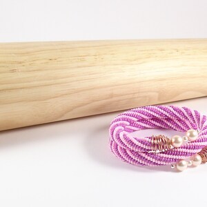 May include: A pink and white beaded necklace with a twisted design and pearl accents. The necklace is made with small beads and has a delicate, feminine look.