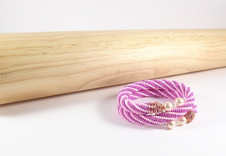 May include: A pink and white beaded necklace with a twisted design and pearl accents. The necklace is made with small beads and has a delicate, feminine look.