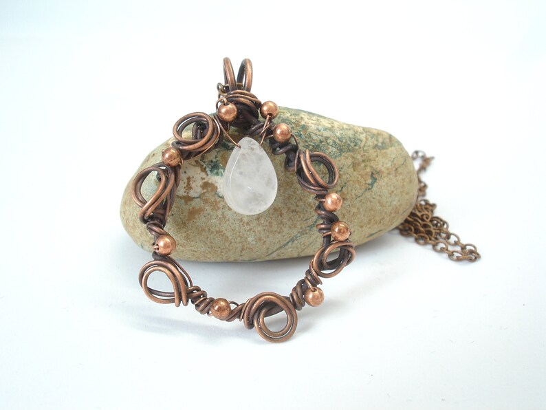May include: A copper wire wrapped pendant with a clear quartz teardrop charm. The pendant is hanging from a copper chain.