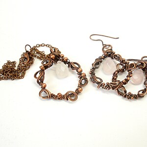 May include: A set of copper wire earrings and a necklace with rose quartz stones. The earrings are made of three intertwined circles with a rose quartz stone hanging from each circle. The necklace is a single circle with a rose quartz stone hanging from the bottom.