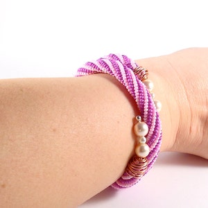 May include: A pink and white beaded bracelet with gold accents and white pearl beads.