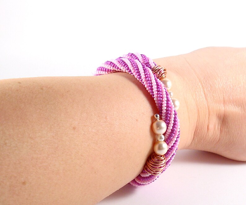 May include: A pink and white beaded bracelet with gold accents and white pearl beads.