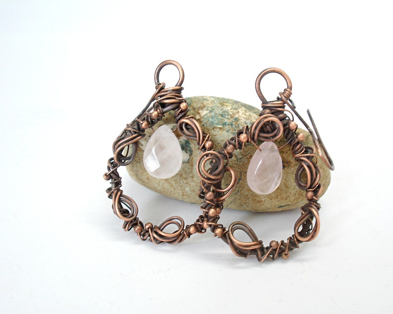 May include: A pair of copper wire earrings with rose quartz drops. The earrings are made of twisted copper wire and have a delicate, intricate design.