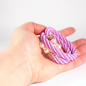 May include: A pink and white beaded bracelet with pearl accents. The bracelet is made of small beads woven together in a spiral pattern.