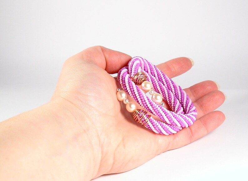 May include: A pink and white beaded bracelet with pearl accents. The bracelet is made of small beads woven together in a spiral pattern.
