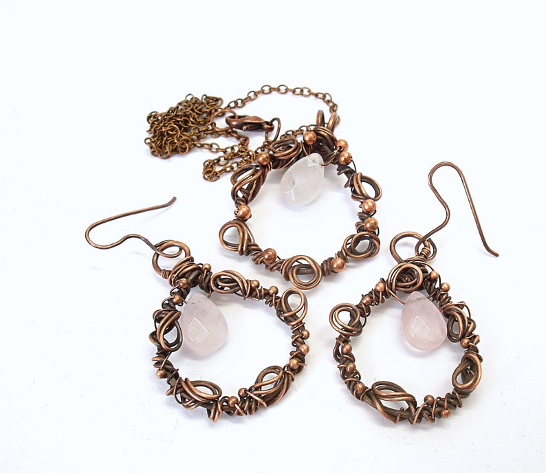 May include: A copper wire wrapped necklace and earrings set with rose quartz stones. The necklace has a delicate chain and the earrings have a teardrop shape.