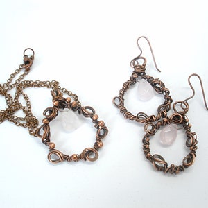 May include: A set of copper wire earrings and a necklace with pink rose quartz stones. The earrings and necklace feature a delicate, intricate design.