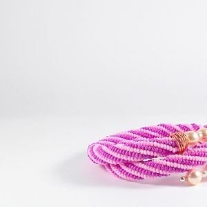 May include: A pink and white beaded necklace with gold wire accents and pearl beads.