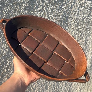 May include: A brown ceramic serving tray with a woven design and two handles. The tray is oval shaped and has a rustic look.